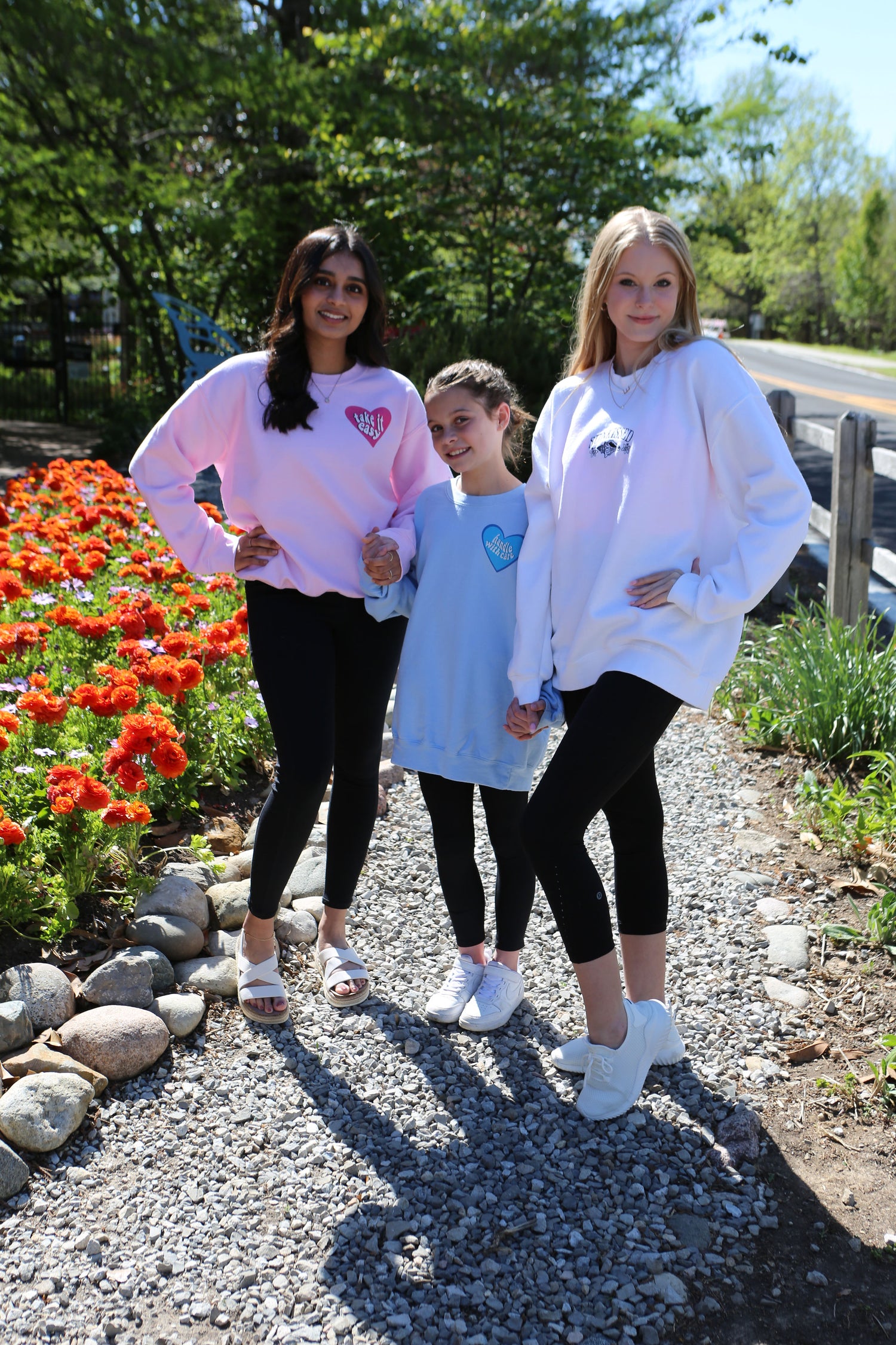 three girls wearing trendy crewneck sweatshirts standing by flowers